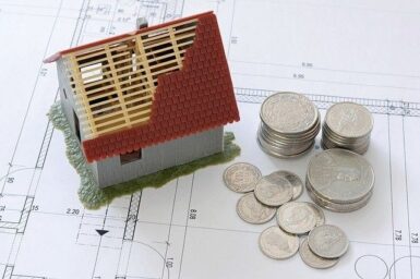 Photo d'une maison miniature posé sur un plan et quelques pièces de monnaies