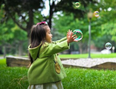 Petite fille au manteau vert jouant avec une bulle de savon